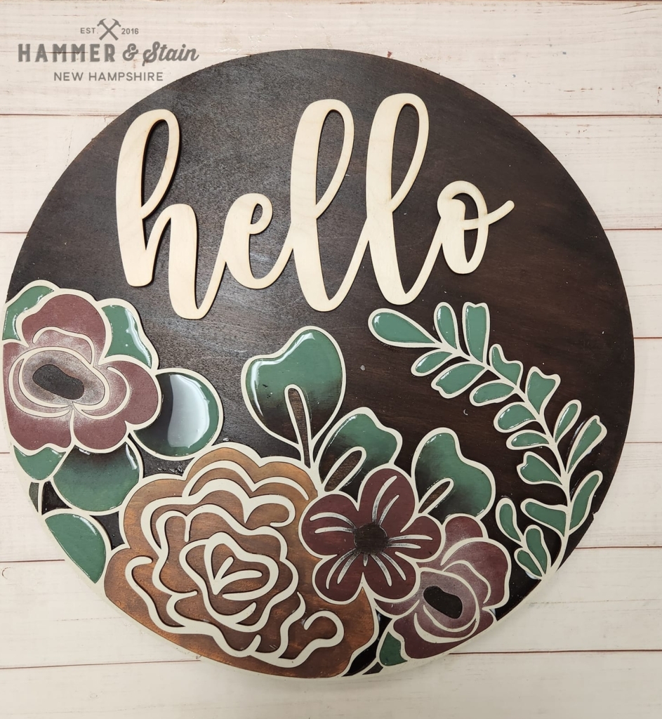 A round wooden sign with flowers on it.